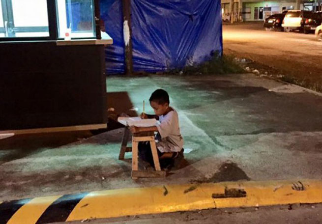 Piše domaći na cesti uz svjetla obližnjeg restorana 